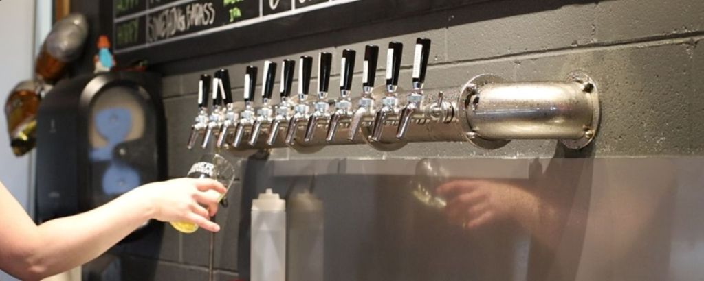 A bartender pouring beer from a row of draft taps mounted on a wall, highlighting a modern beverage dispensing system.